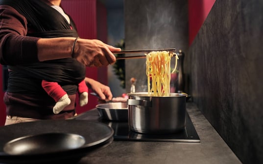 Man cooking spaghetti on a hob.