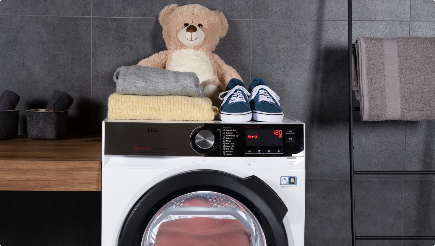 Teddy bear, sweaters and a pair of shoes placed on top of an AEG washing machine .